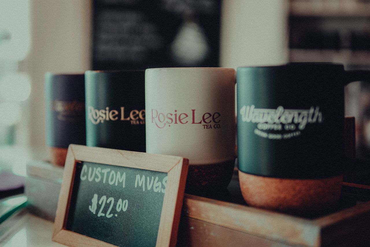 digital Close-up of custom coffee mugs in a cafe with a price sign, highlighting product details.